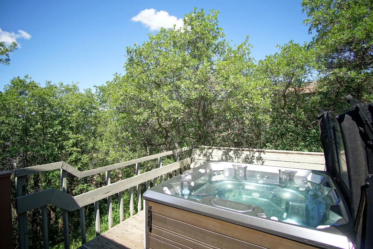 An exterior view highlighting the chalet’s hot tub and surrounding trees on the deck. The angle emphasizes the serene outdoor space, ideal for group socializing, listening to nature, or stargazing in the evenings.