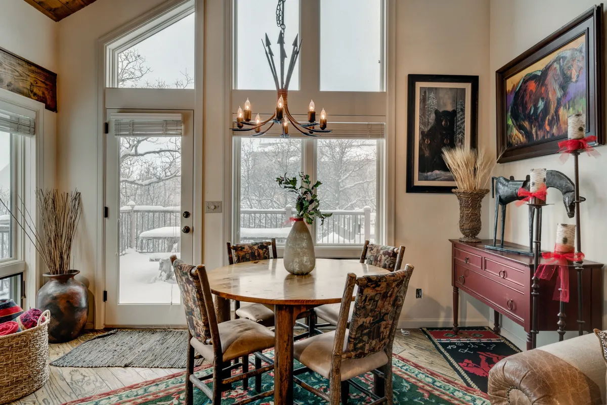 An open-concept dining area with a large table, elegant chandelier, expansive windows, and tasteful artwork. The bright, airy room is set for family meals, laughter, and celebrations, while the windows frame serene outdoor views.