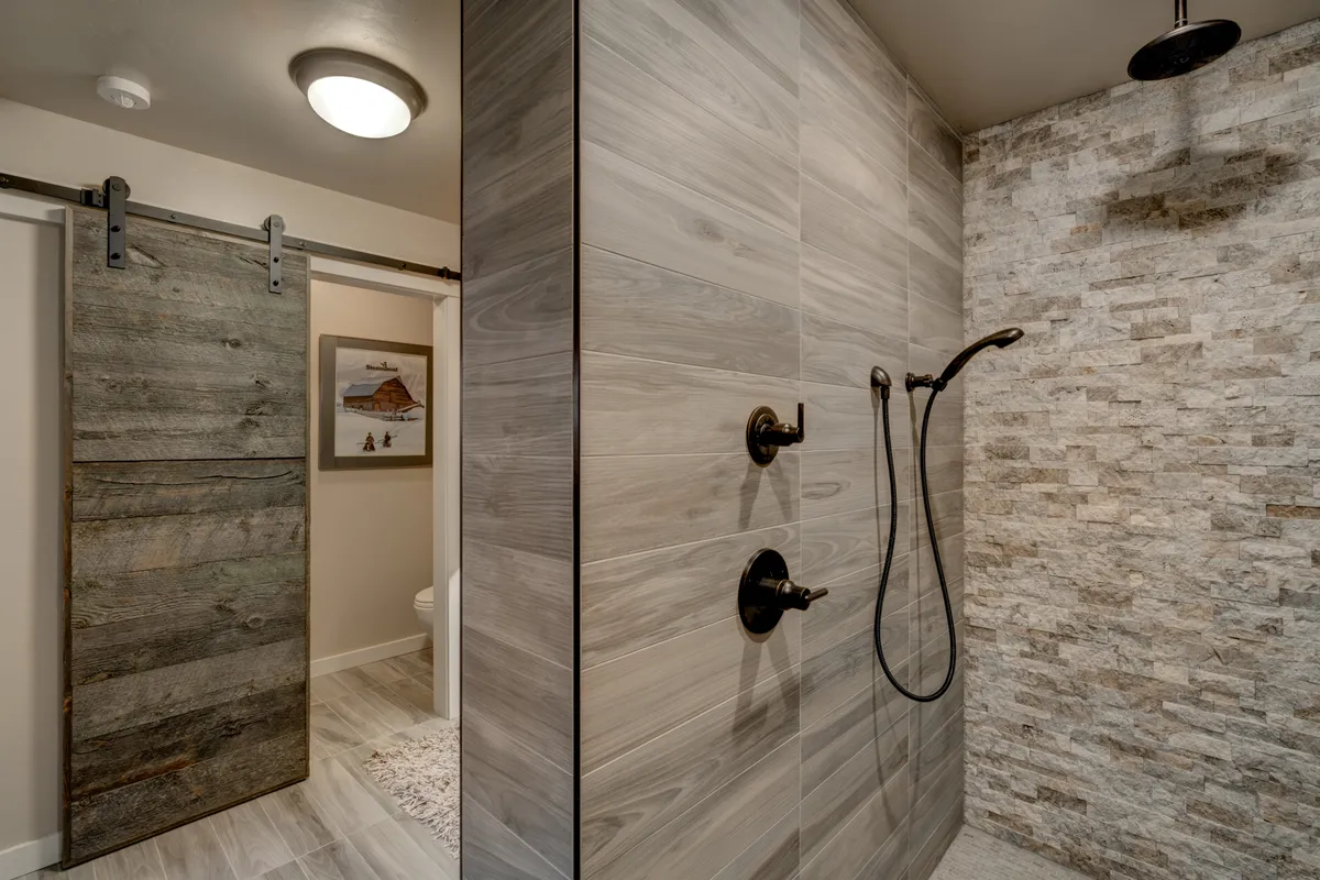A modern shower area with elegant stone walls, sleek shower fixtures, and a prominent sliding barn door—evoking the spa-like ambiance described in the section. The thoughtful design elements create an atmosphere of tranquility and indulgence.