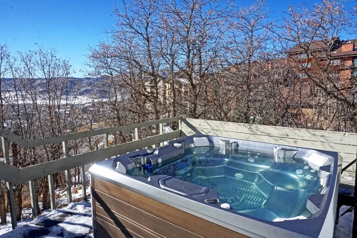 An inviting exterior scene featuring a private hot tub on the deck, surrounded by trees and boasting an open mountain view. The setup suggests a perfect après-ski experience, ideal for relaxing after a day on the slopes while soaking in the scenery.