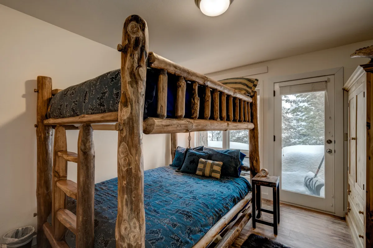 A welcoming bedroom with a bunk bed, blue bedding, and wooden furnishings. The window highlights a snowy landscape outside, reminding guests of the mountain environment just beyond the chalet.