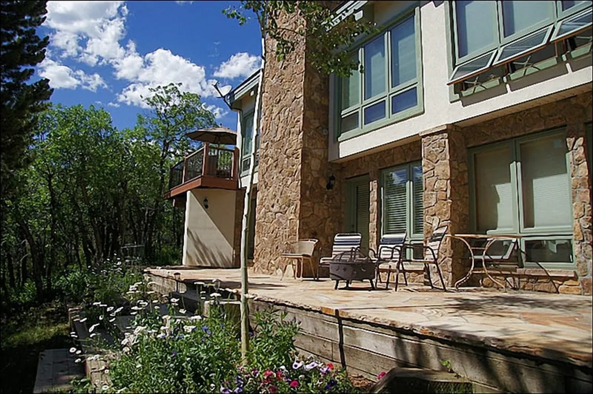 A wraparound wooden deck with outdoor seating, surrounded by lush greenery and offering ample space to relax or entertain. The deck is an inviting transition between the indoors and outdoors, perfect for grilling or sipping drinks while enjoying the view.