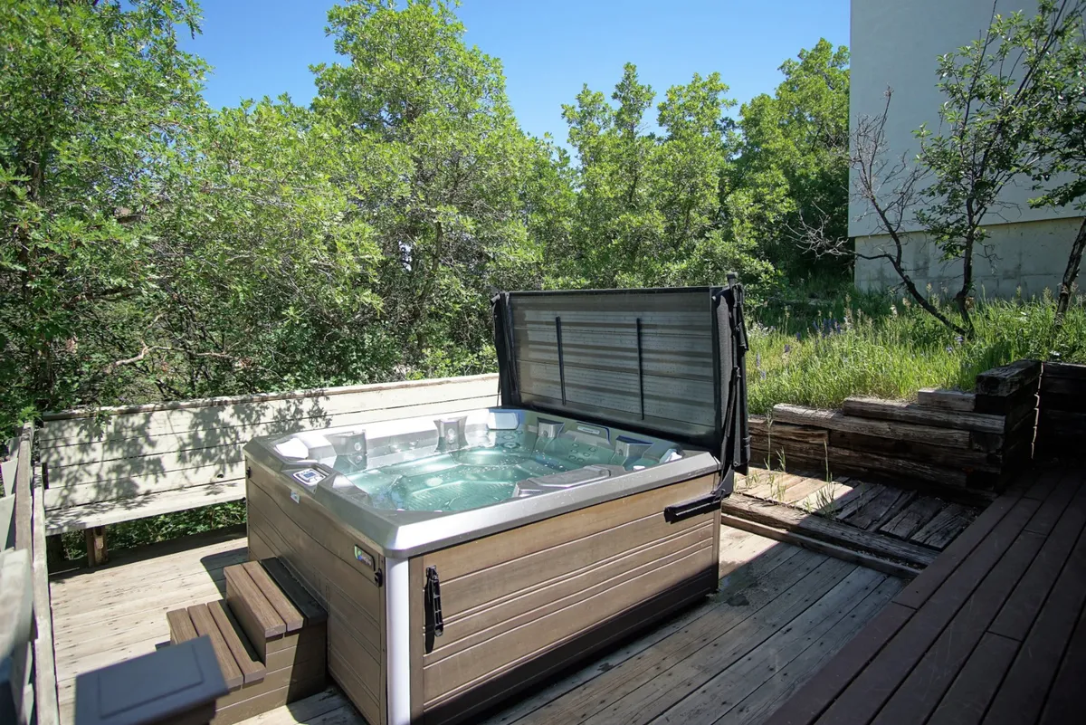 This image features a private hot tub nestled amidst lush greenery, set on a deck that invites relaxation. The scene is tranquil, with the hot tub as the focal point, surrounded by natural beauty, suggesting the perfect place for an après-ski soak or a serene morning routine.