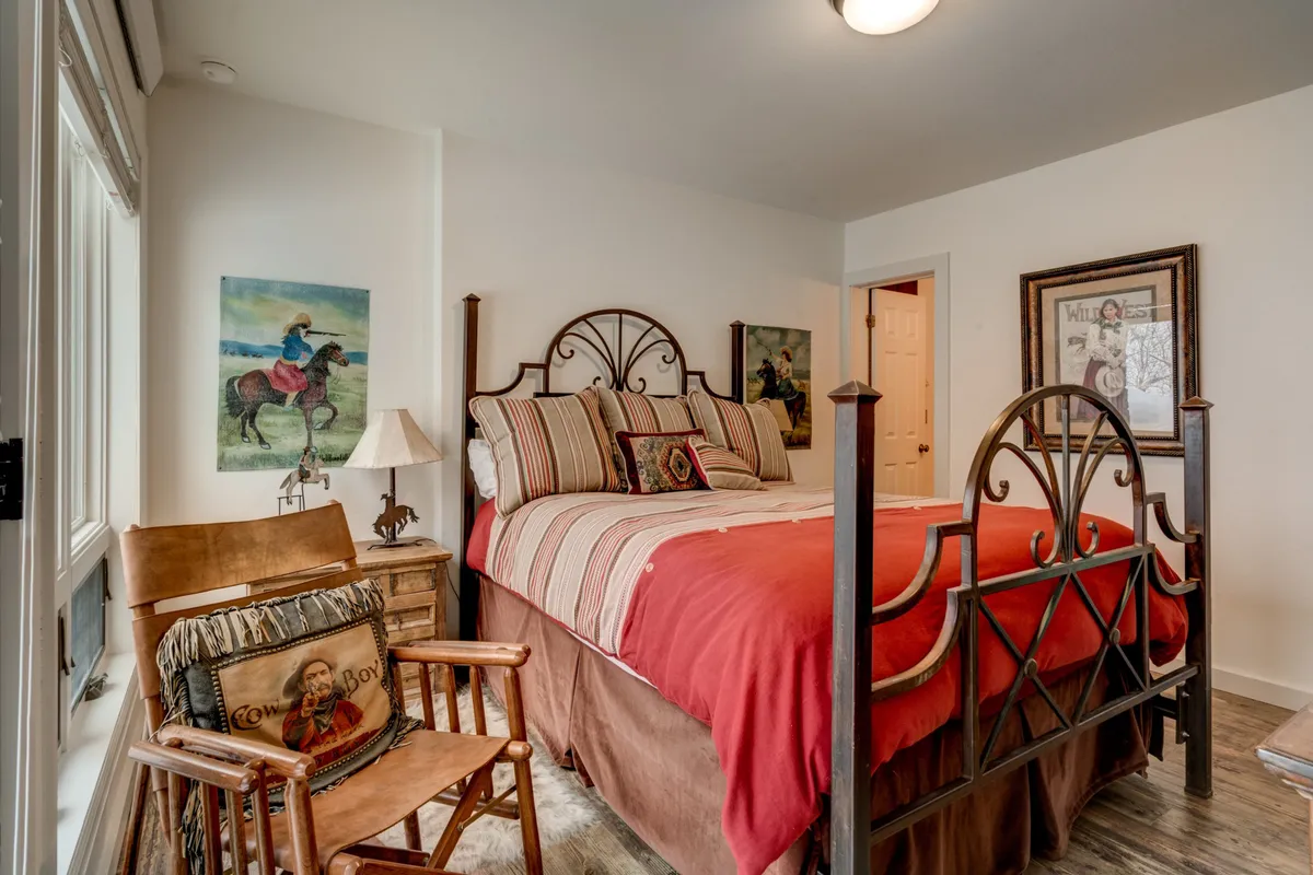 This image showcases a cozy bedroom featuring a bed with rich red bedding, a comfortable armchair accented by decorative pillows, and tasteful artwork on the walls. The setting exudes warmth and provides an inviting atmosphere—ideal for relaxing after a day of exploring the outdoors.