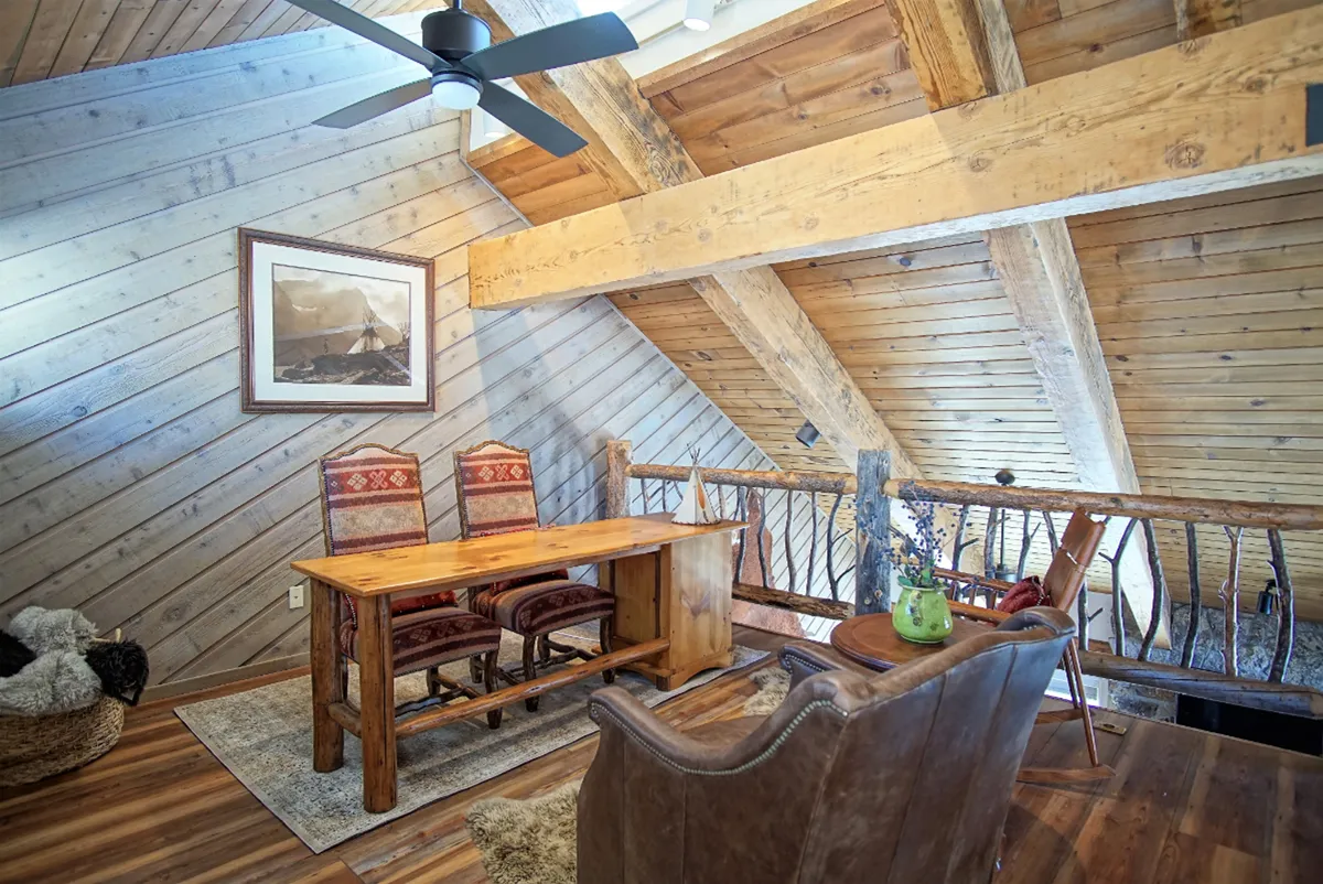A warm, inviting interior scene featuring a wooden table with two chairs, artwork, and a fan. The setting suggests a space for sharing meals, holding conversations, or enjoying quiet moments together, evoking home-cooked family dinners and storytelling.