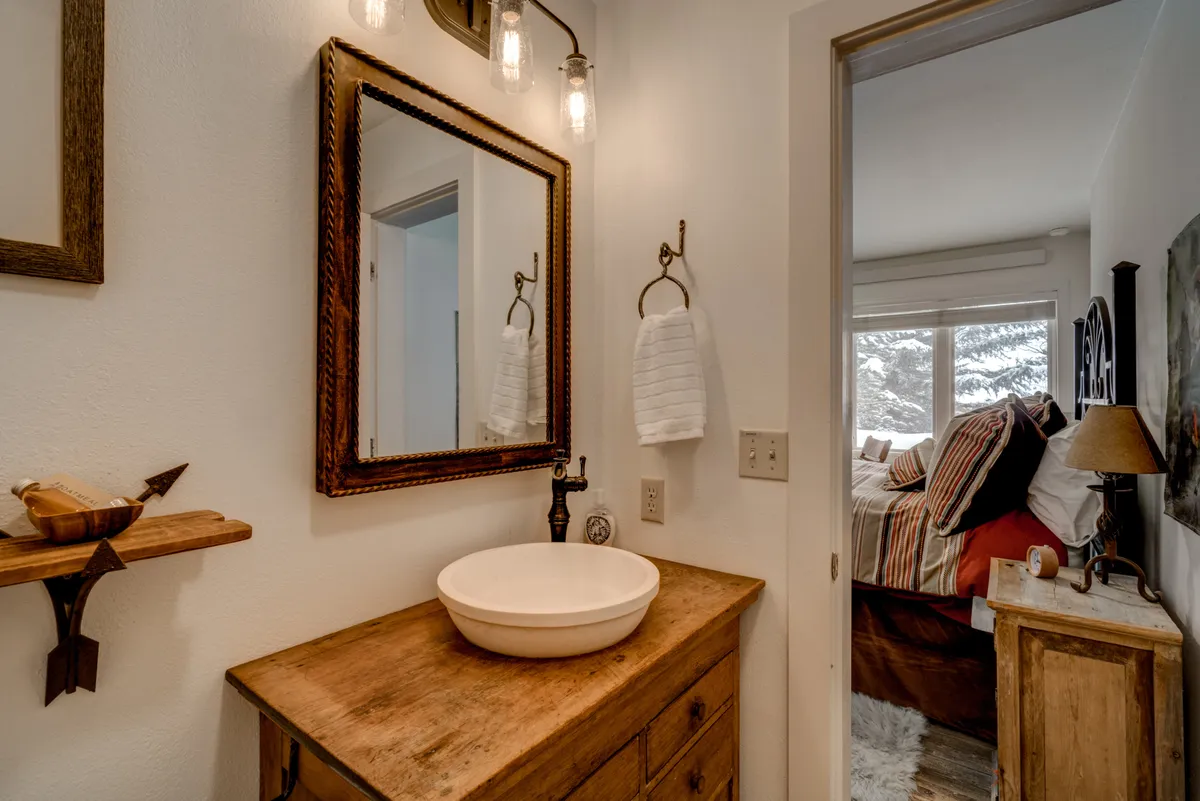 A stylish bathroom featuring a vintage wooden vanity, a round basin sink, a decorative mirror, and soft towels. The design blends rustic charm with spa-inspired details, suggesting a space for pampering and unwinding.