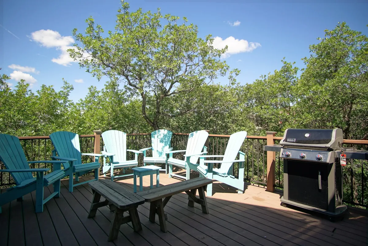 A cozy patio setup with turquoise Adirondack chairs and a grill is showcased, suggesting an inviting space for gatherings or a quiet morning coffee. The seating area is open to nature, reinforcing the idea of outdoor living and relaxation.